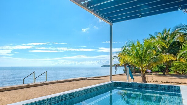 A clear blue sky, a swimming pool with blue tiles, a beach, and palm trees. - Entire Beach Home w/ Sunroom, Pool, Bikes, Paddleboards, BBQ & more (Hopkins)