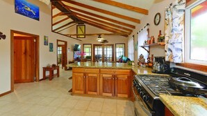 A spacious kitchen with a large island, wooden cabinets, a stove, and a window with curtains. - Entire Beach Home w/ Sunroom, Pool, Bikes, Paddleboards, BBQ & more (Hopkins)