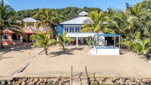 A beachfront property with a pool, palm trees, and a covered area. - Entire Beach Home w/ Sunroom, Pool, Bikes, Paddleboards, BBQ & more (Hopkins)