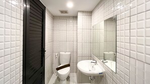 Un baño moderno con paredes de azulejos blancos, una puerta negra, un inodoro y un lavabo con espejo.
