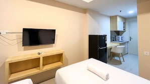 Una habitación de hotel con cama, televisor montado en la pared, estante de madera, kitchenette y una silla.