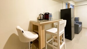 A small kitchen with a wooden table, a white chair, a black refrigerator, and a grey armchair. - Comfortable And Nice 2Br Apartment At Meikarta (Cikarang)