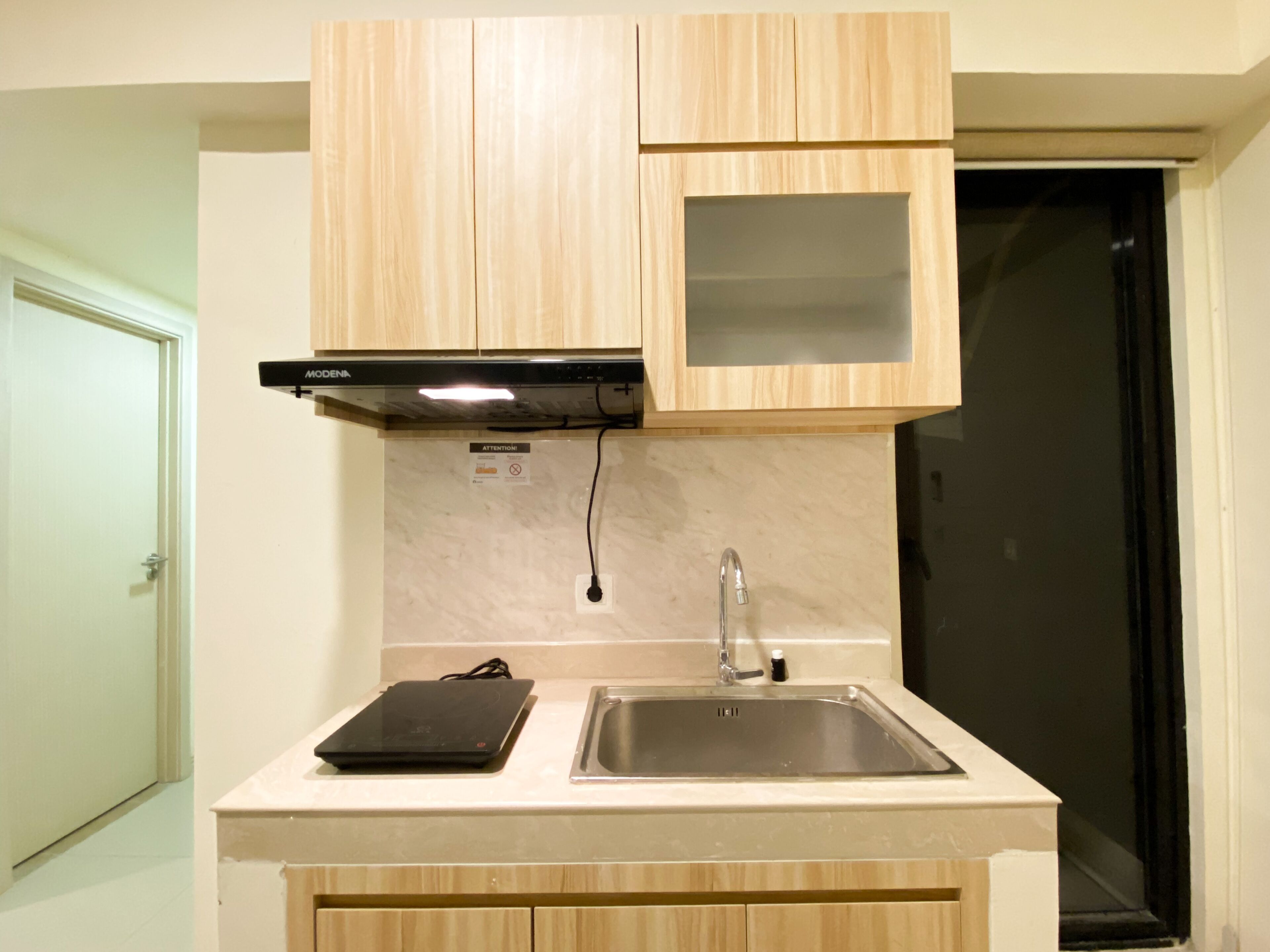 Une cuisine avec des meubles de rangement en bois, une plaque de cuisson à induction noire, un évier en acier inoxydable et un réfrigérateur noir.