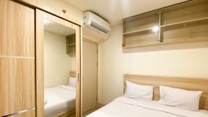 A hotel room with a wooden wardrobe, a bed with white bedding, and an air conditioning unit mounted on the wall. - Comfortable And Nice 2Br Apartment At Meikarta (Cikarang)