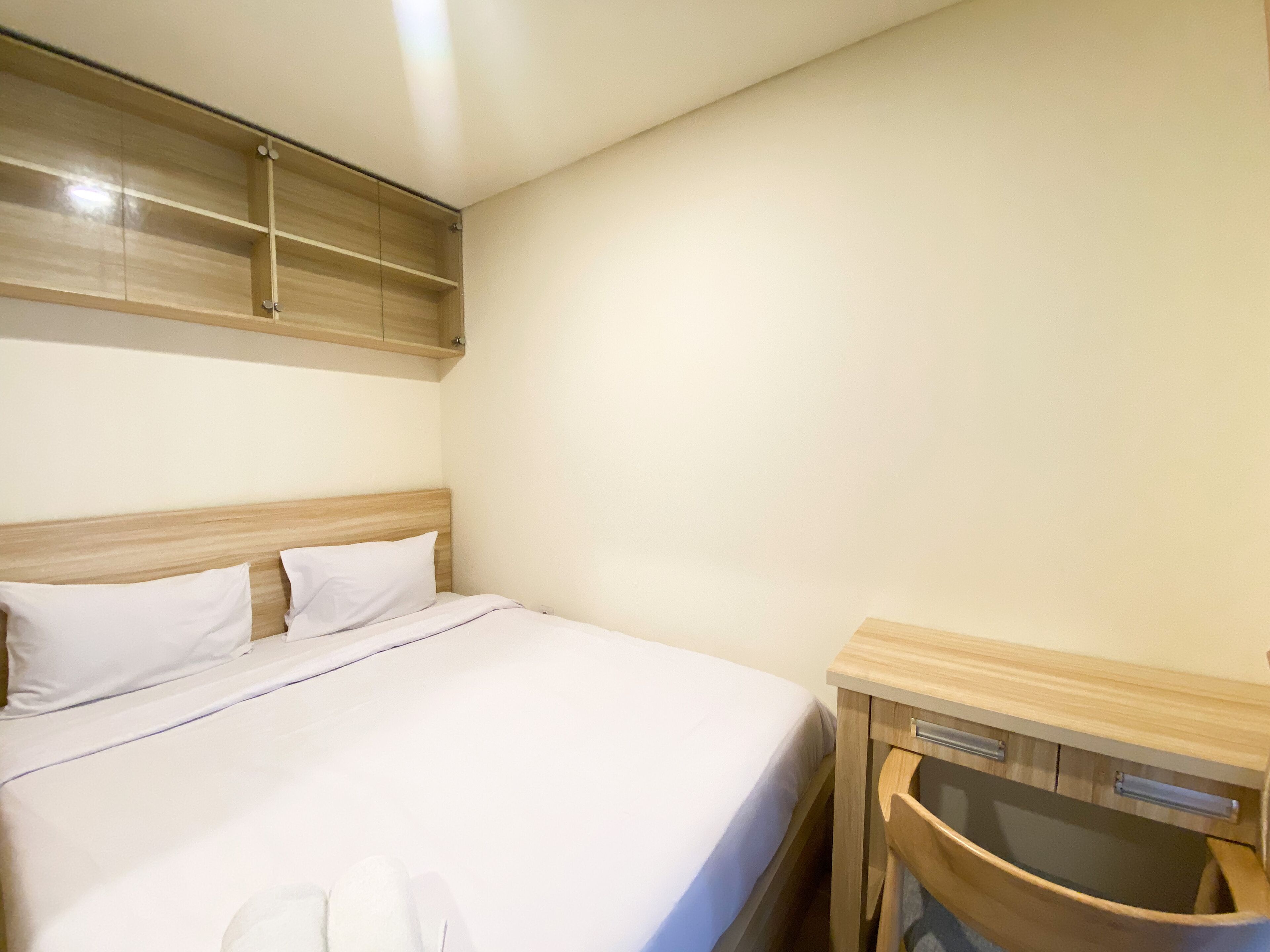 A hotel room with a bed, a wooden headboard, a wooden nightstand with a drawer, and a wall-mounted cabinet.