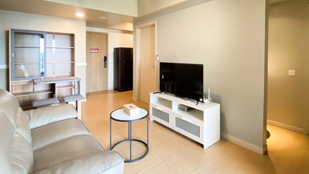 A modern living room with a sofa, TV stand, and a small round table. - Comfort Stay And Simply 2Br At Meikarta Apartment (Cikarang)