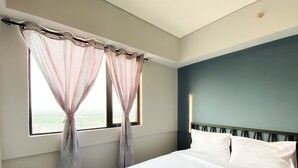 A bedroom with a bed, two windows with sheer curtains, a headboard, and a view of the outdoors. - Comfort Stay And Simply 2Br At Meikarta Apartment (Cikarang)