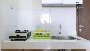 A kitchen with white tiles, a gas stove, a sink, and a green dish rack. - Good Deal 2Br At 16Th Floor Suites @Metro Apartment (Bandung)