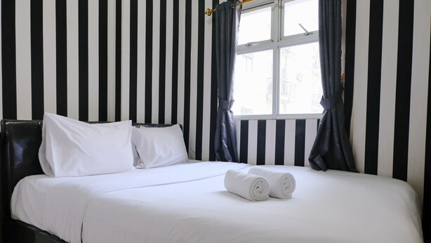 A neatly made bed with white linens, a black headboard, and a window with curtains. - Good Deal 2Br At 16Th Floor Suites @Metro Apartment (Bandung)