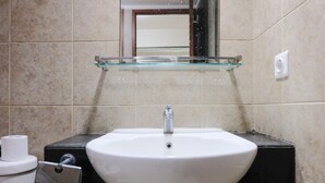 A bathroom with a white sink, a glass shelf above it, and a toilet with a paper towel holder. - Simply 2Br (No Kitchen) At Apartment Marbella Suites Dago Pakar Bandung (Bandung)