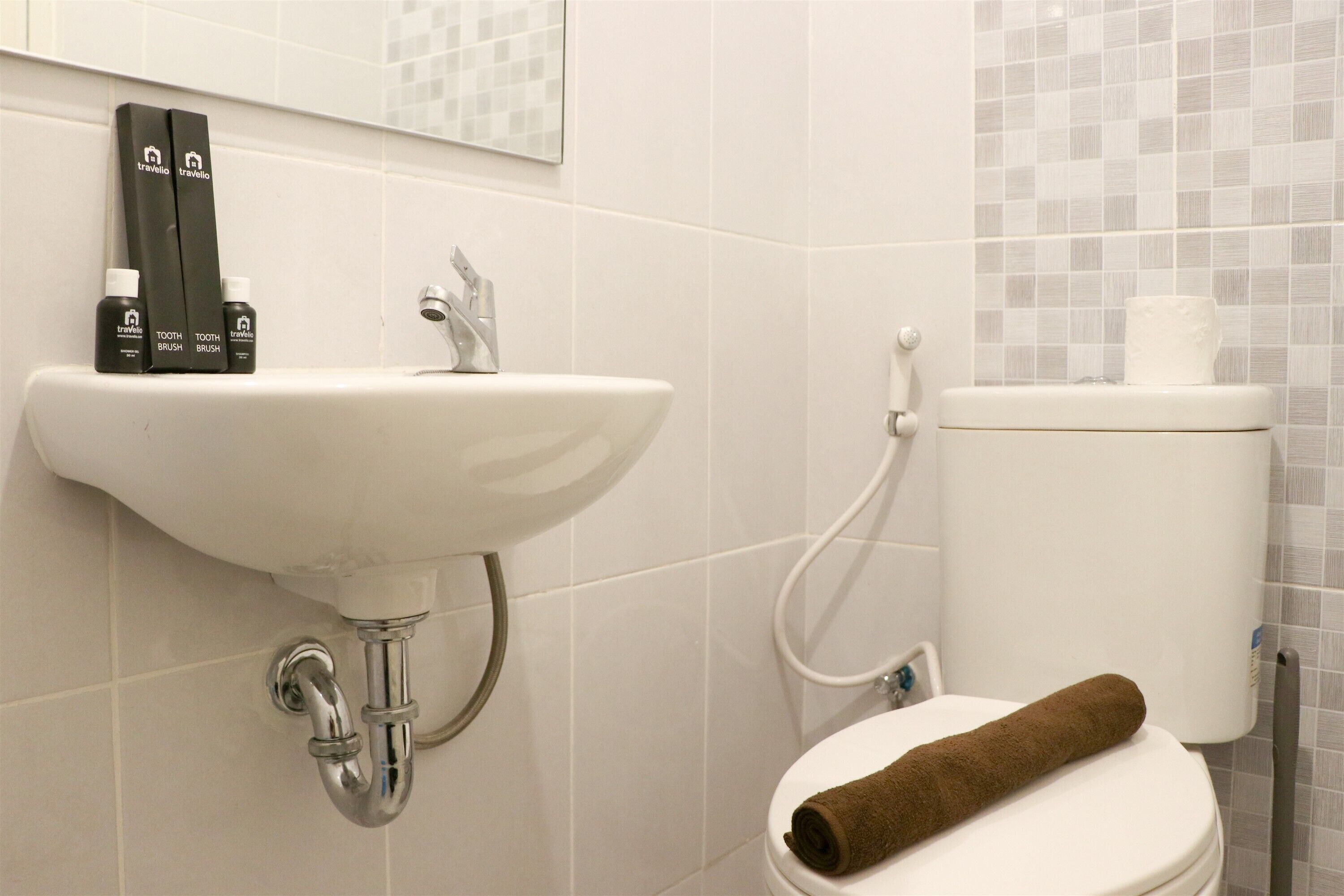 Ein Badezimmer mit einem weißen Waschbecken, zwei Zahnbürsten und einer Toilette, auf der ein braunes Handtuch liegt.