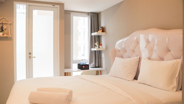 Ein Hotelzimmer mit einem großen Bett, einem Nachttisch, einem Fenster mit Vorhängen und einer Tür.