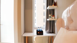 Ein Hotelzimmer mit Bett, Schreibtisch mit Stuhl, Fenster mit Vorhängen und Ablagefläche mit Toilettenartikeln.