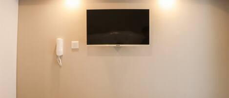 A hotel room with a bed, a wall-mounted TV, a telephone, and a rolled-up towel on the bed.