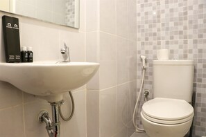 A bathroom with a white sink, a mirror, toiletries, and a toilet. - Nice And Homey Studio Tokyo Riverside Pik 2 Apartment (Teluknaga)