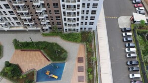 A high-rise residential building with multiple balconies, a parking area, and a small park with a playground. - Nice And Homey Studio Tokyo Riverside Pik 2 Apartment (Teluknaga)
