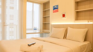 A hotel room with a bed, a remote control, and a neatly folded towel. - Nice And Homey Studio Tokyo Riverside Pik 2 Apartment (Teluknaga)