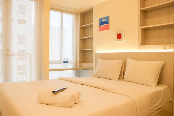 A hotel room with a bed, a remote control, and a neatly folded towel. - Nice And Homey Studio Tokyo Riverside Pik 2 Apartment (Teluknaga)