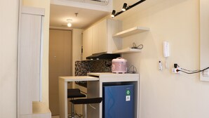 A compact kitchen with a refrigerator, a microwave, and a sink. There are two bar stools and a countertop. - Nice And Homey Studio Tokyo Riverside Pik 2 Apartment (Teluknaga)