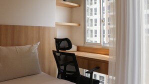 A hotel room with a bed, a desk with a chair, a window with curtains, and a view of a building outside. - Relaxing Studio Apartment At Tokyo Riverside Pik 2 (Teluknaga)