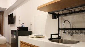 A modern kitchen with a stainless steel sink, a black countertop, and wooden cabinets. - Relaxing Studio Apartment At Tokyo Riverside Pik 2 (Teluknaga)