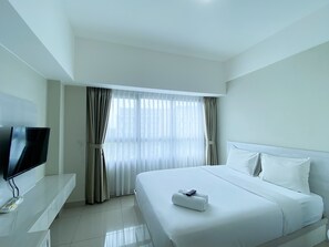 A hotel room with a bed, a TV on a stand, and a window with curtains. - Restful And Simply Studio Springlake Summarecon Bekasi Apartment (Bekasi)