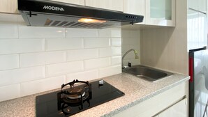A kitchen with white cabinets, a stainless steel sink, and a black induction cooktop. - Restful And Simply Studio Springlake Summarecon Bekasi Apartment (Bekasi)