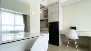 A modern hotel room with a white desk, a black refrigerator, a white chair, and a minibar. - Restful And Simply Studio Springlake Summarecon Bekasi Apartment (Bekasi)