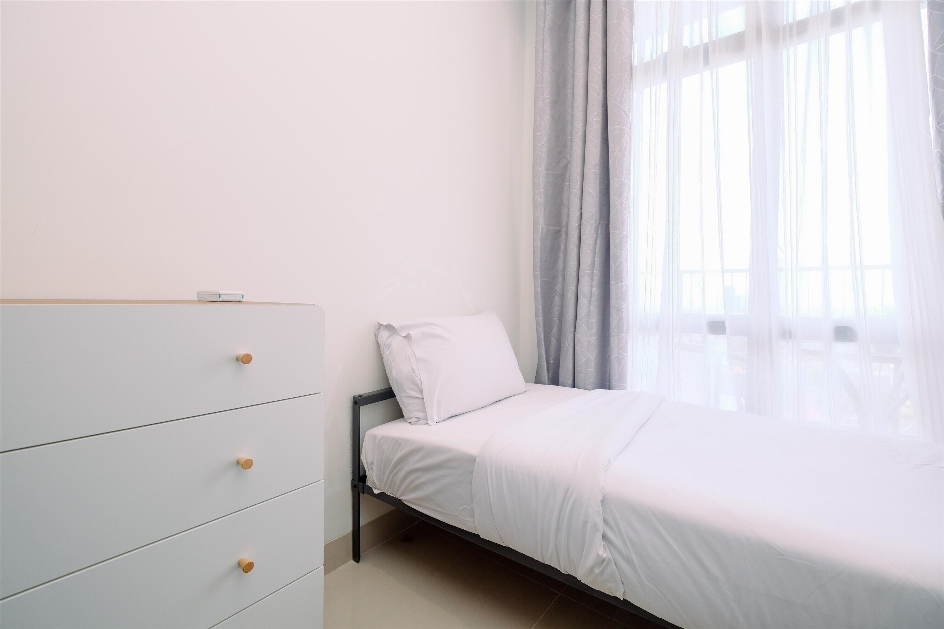 A bedroom with a bed, a white dresser with drawers, and a window with sheer curtains.
