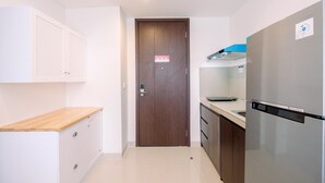 A compact kitchen with white cabinets, a wooden countertop, a stainless steel refrigerator, and a brown door.