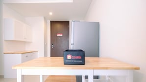 A small kitchenette with a wooden table, a refrigerator, and a travel bag on the table.