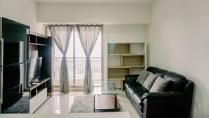 Un salon moderne avec un canapé en cuir noir, une table basse en verre, un téléviseur à écran plat posé sur un meuble en bois et une grande fenêtre ornée de rideaux légers.