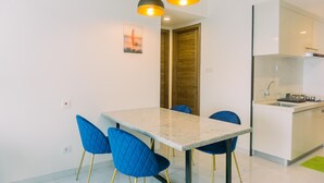 A modern kitchen with a marble countertop, a sink, and a built-in oven. There are blue chairs around a rectangular dining table. - Comfort And Modern Look 3Br Sky House Bsd Apartment (Pagedangan)