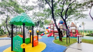 A playground with colorful play structures, including slides and climbing areas, surrounded by trees and a paved walkway. - Comfort And Modern Look 3Br Sky House Bsd Apartment (Pagedangan)