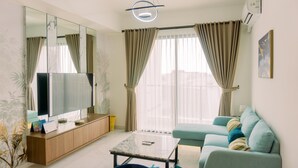 A modern living room with a flat-screen TV, a sofa, a coffee table, and a large window with curtains. - Comfort And Modern Look 3Br Sky House Bsd Apartment (Pagedangan)