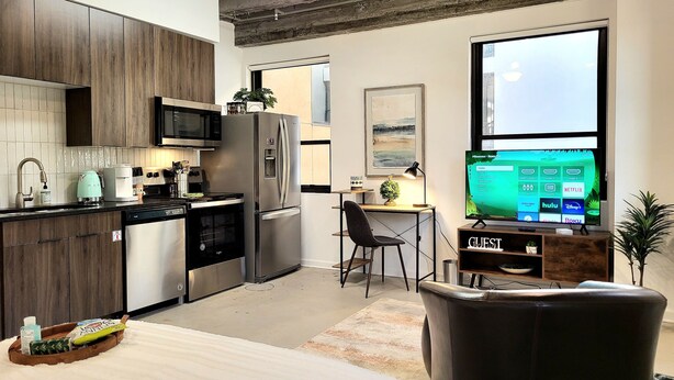 Cocina moderna con refrigerador, microondas y estufa. Hay un comedor con mesa y sillas, y un televisor montado en la pared mostrando servicios de transmisión.