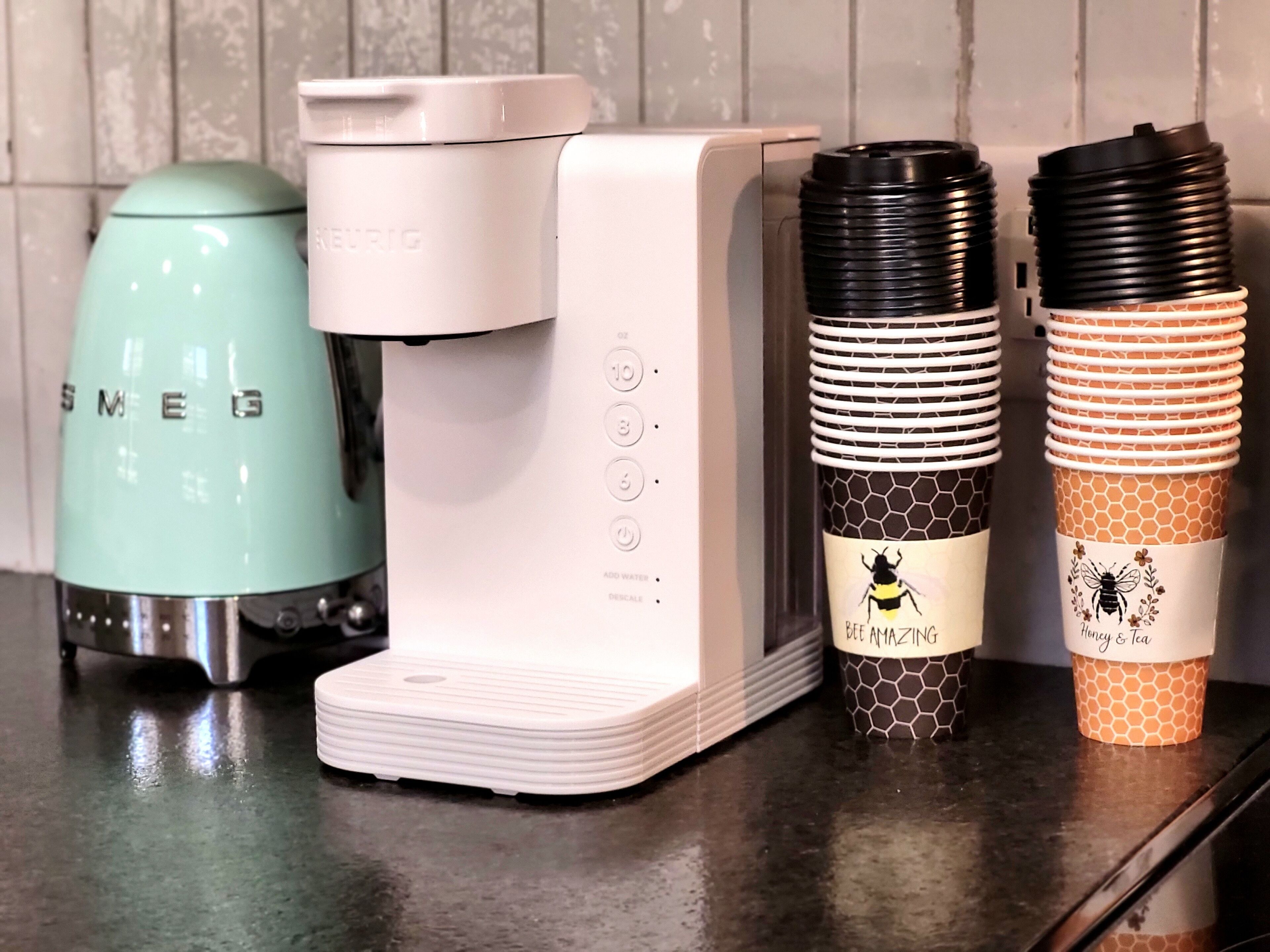 Una cucina con una macchina del caffè color petrolio, una macchina del caffè bianca e due tazze a nido d'ape con motivi di api.