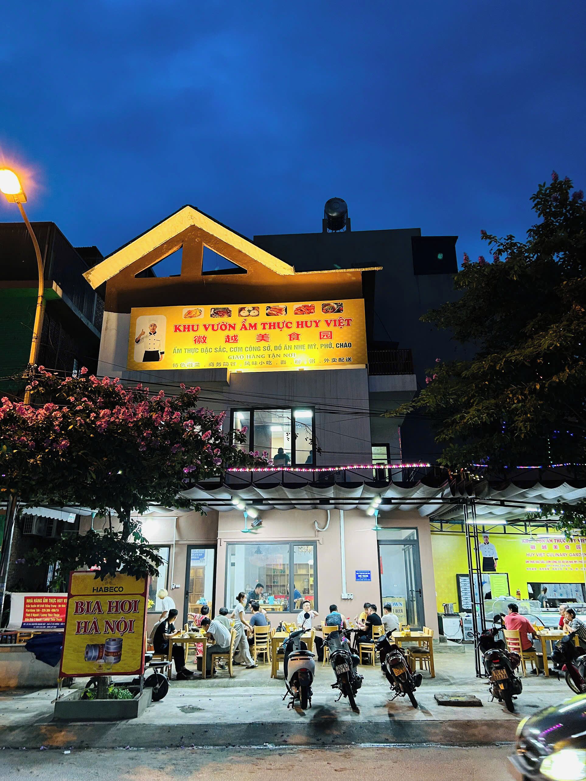 A restaurant with outdoor seating, a signboard advertising food, and a few parked motorcycles.