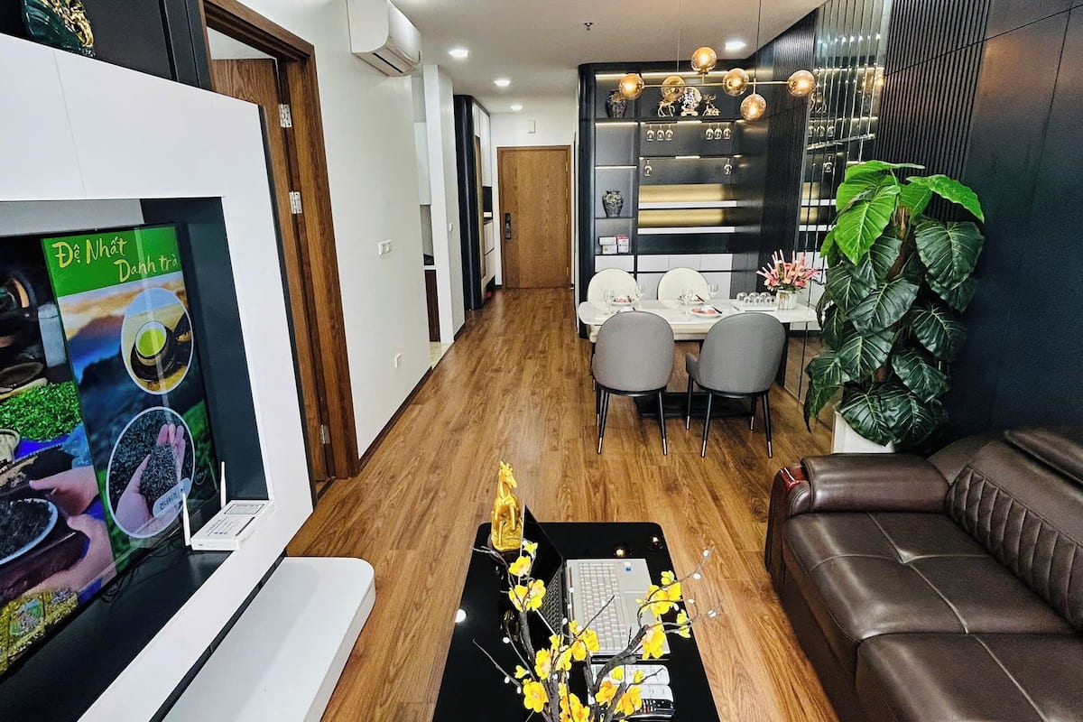 A modern living room with a black coffee table, a brown leather sofa, and a dining area with a chandelier.