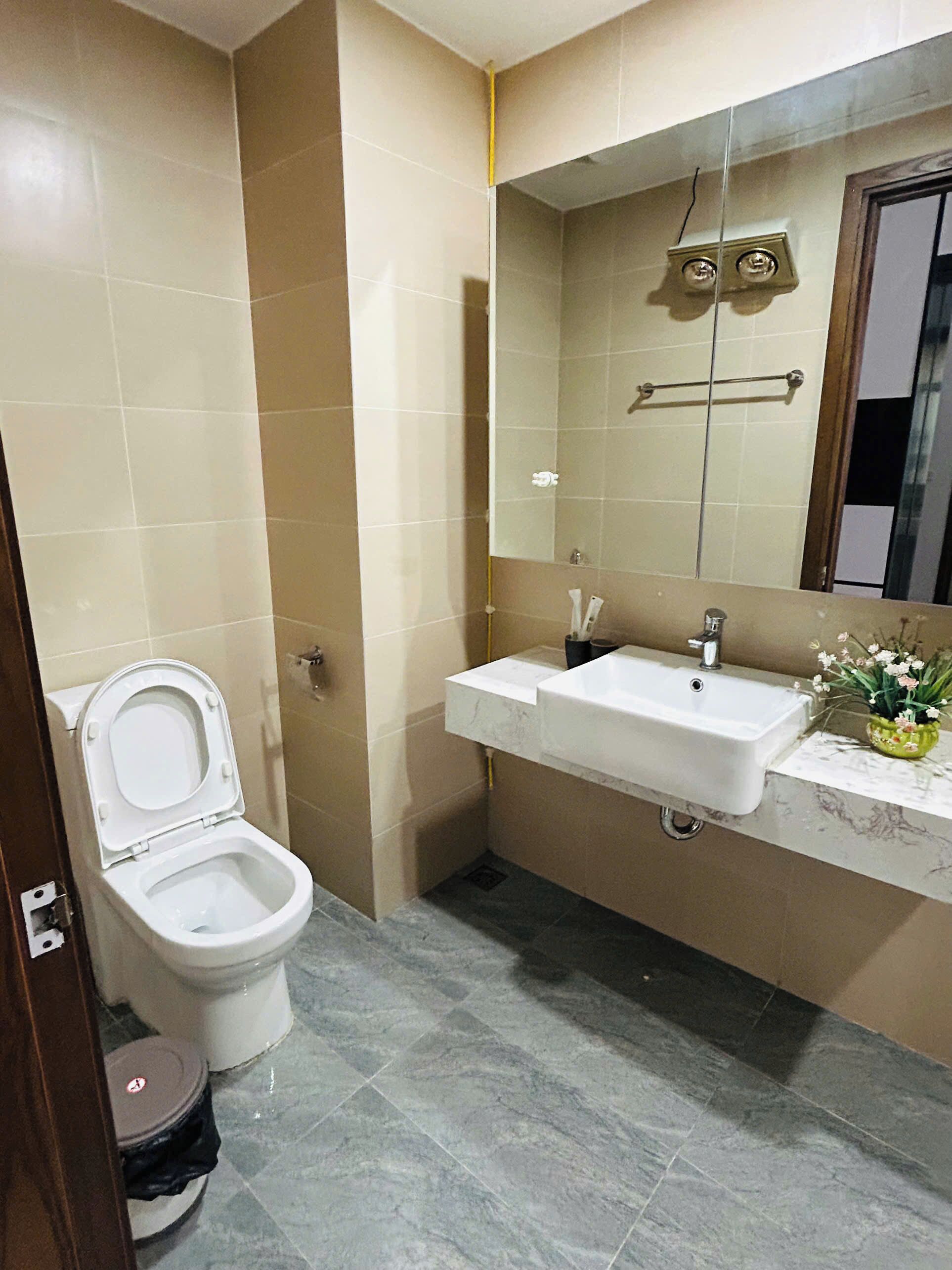 A bathroom with a toilet, sink, mirror, and tiled walls.