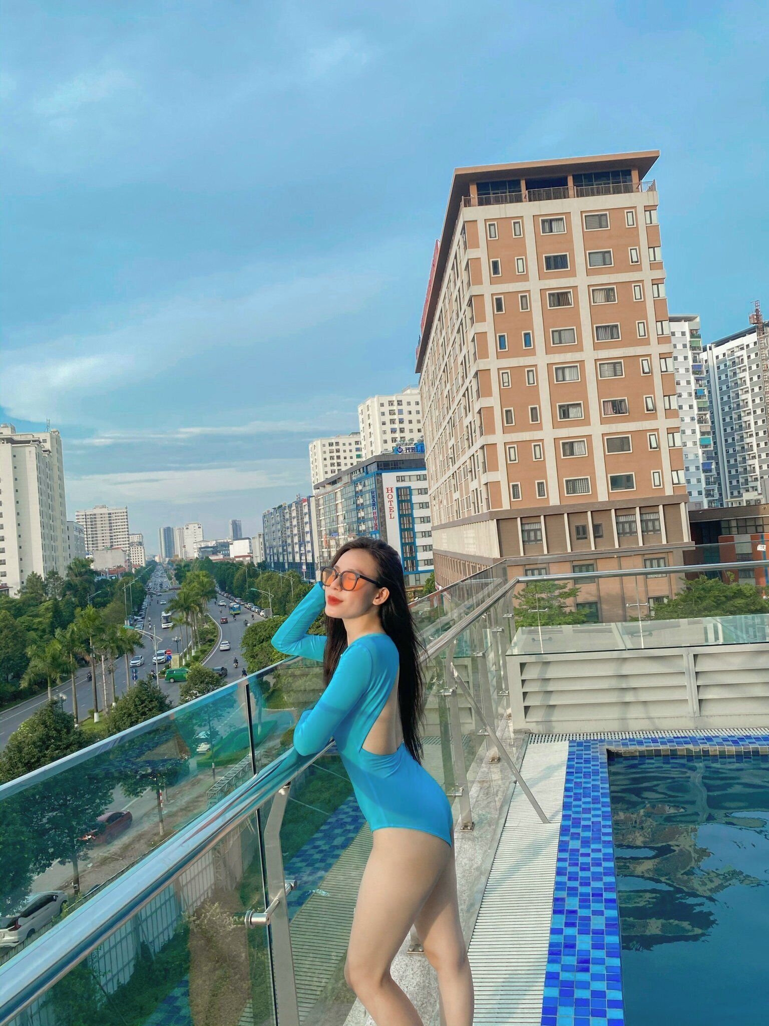 A person standing by a glass railing overlooking a cityscape with modern buildings and a clear sky.