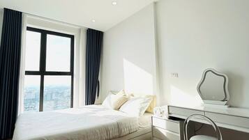 A modern hotel room with a large bed, a desk with a chair, and a view of the city through a large window.