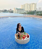 Una persona sentada junto a una piscina, con una mesa de comida y bebidas.