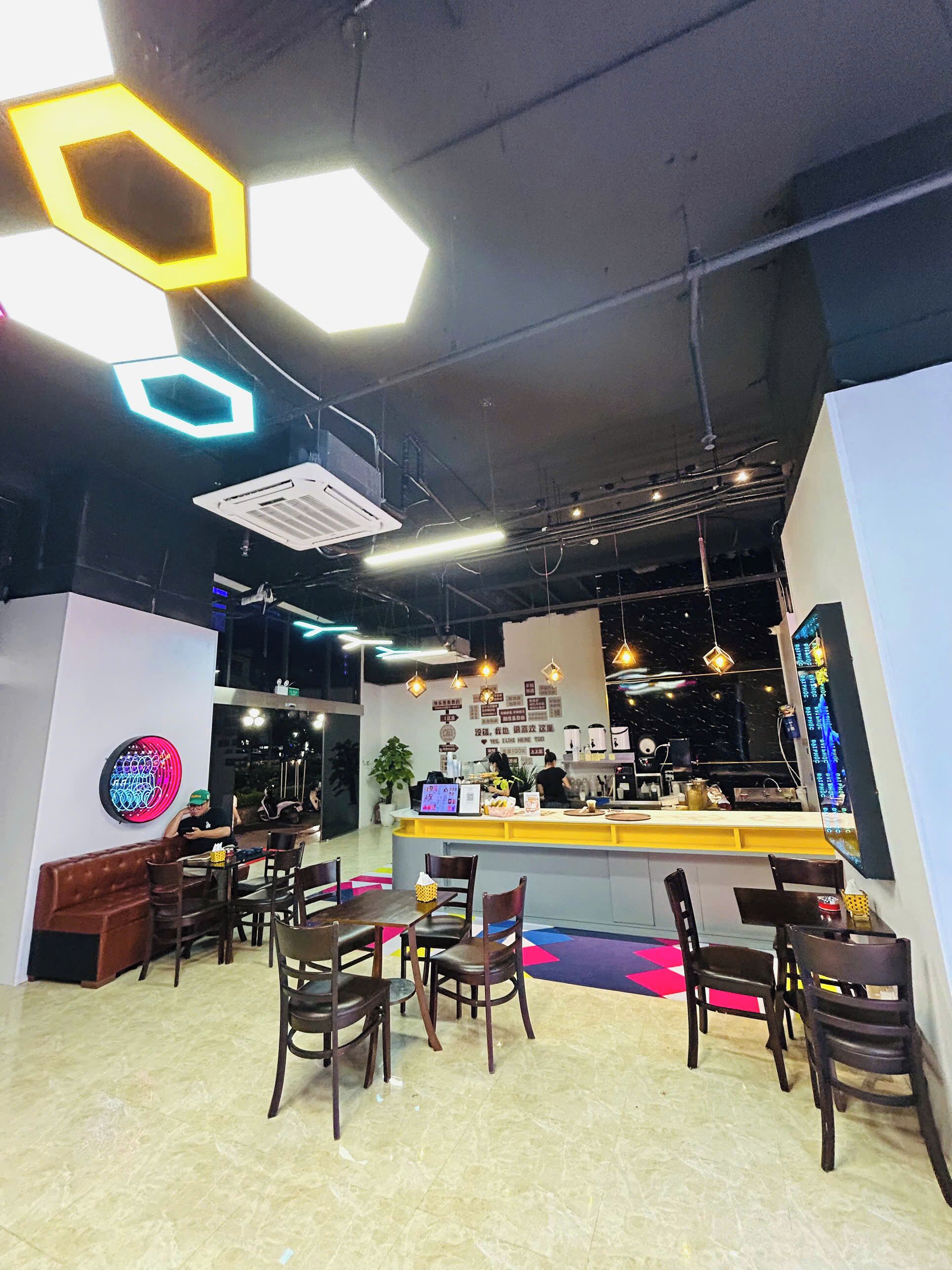 A modern restaurant interior with hexagonal ceiling lights, a central counter, and multiple seating areas.