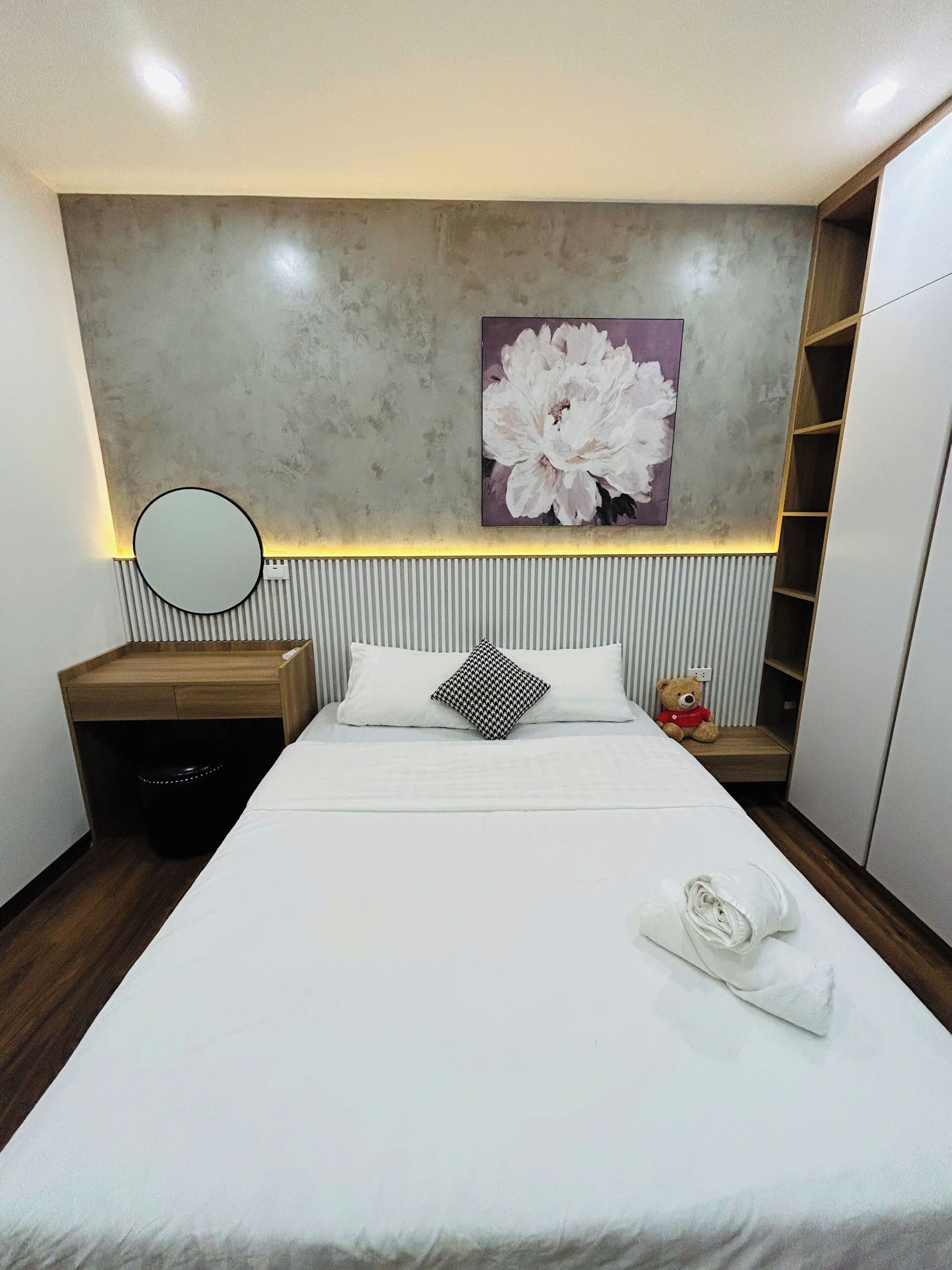A modern bedroom with a large bed, a bedside table, a mirror, a teddy bear, and a wall-mounted shelf.