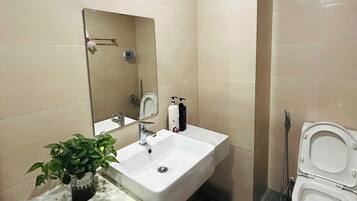 Et badeværelse med hvid vask, spejl, toilet og en potteplante.