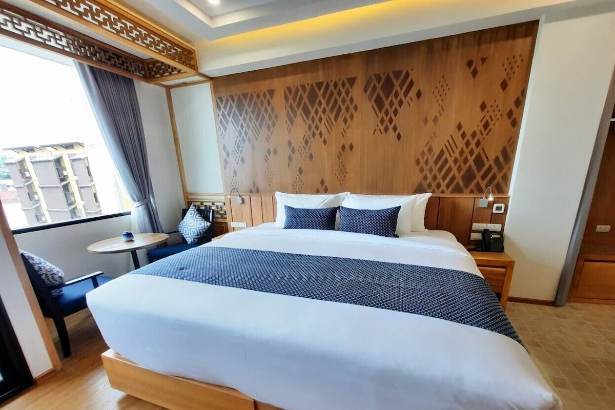 Une chambre d’hôtel avec un grand lit, une petite table, une chaise, une table de chevet et une vue sur l’extérieur.