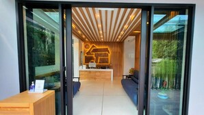 A modern reception area with a wooden reception desk, a seating area with blue sofas, and a reception desk with a logo. - Ama's House Luxury Boutique Hotel (Chiang Mai)