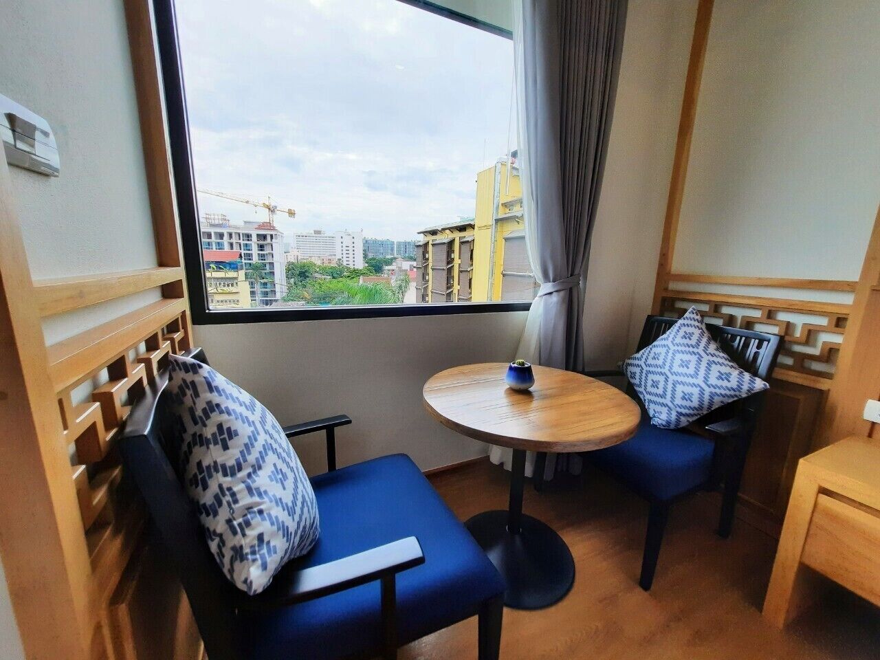 A small room with a wooden-framed window, two blue chairs, a round wooden table, and a small wooden side table.