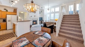 A spacious living area with a fireplace, a dining table with placemats, a staircase, and a kitchen with wooden cabinets. - Kierland Commons Shops & Dining, Hiking, Fitness room, Gated, Heated Pool & Spa + FREE GOLF & MORE! (Scottsdale)